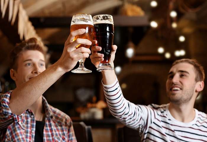 Two male friends toasting beer glasses in a bar
