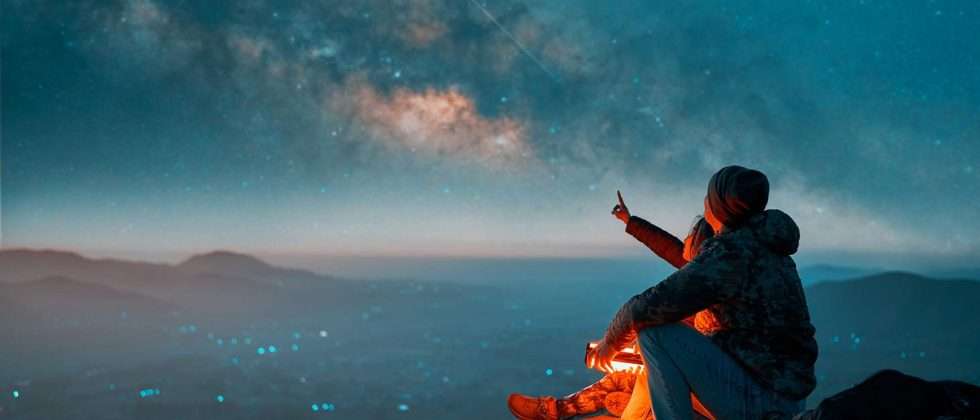 Silhouettes of a latin couple sitting on the top of the hill looking at shooting stars and the milky way in the background