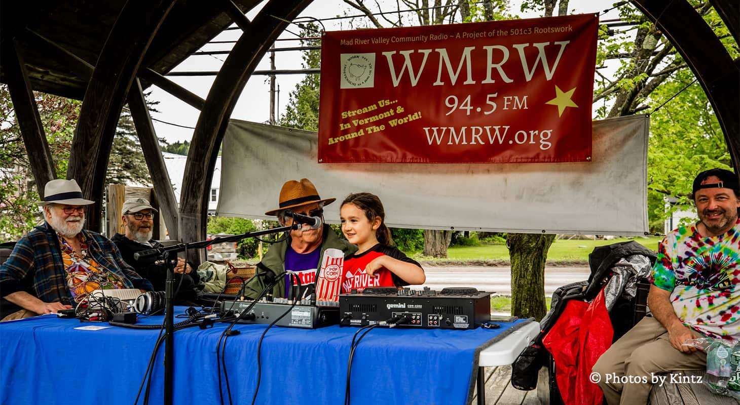 A litttle girl sitting at a table for a local radio station at a Vermont Farmers Market in Waitsfield
