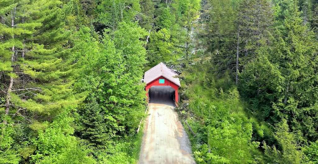 Overhead shot of Moseley Bridge in Vermont, nestled among dense trees, showcasing its rustic charm.