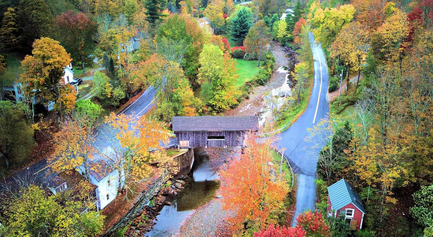 Overhead view of a small town showcasing a bridge and dense tree cover, highlighting the community's layout.