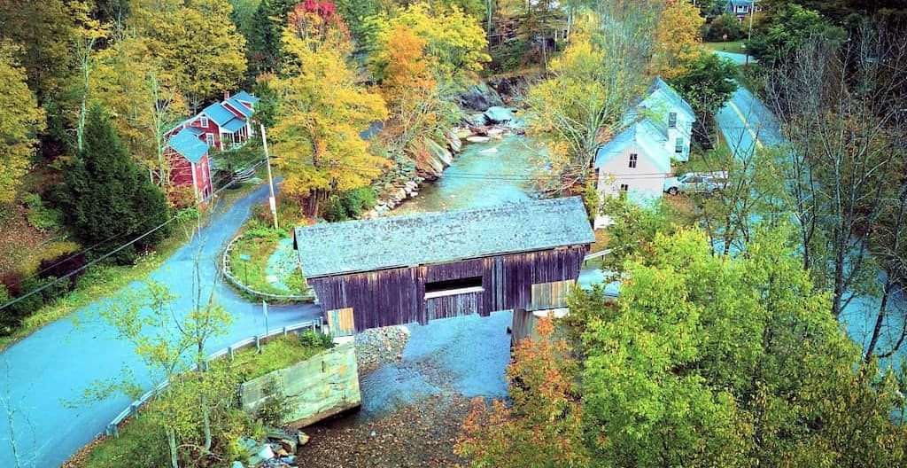 Aerial view of a covered bridge in Warren, Vermont, surrounded by vibrant fall foliage.