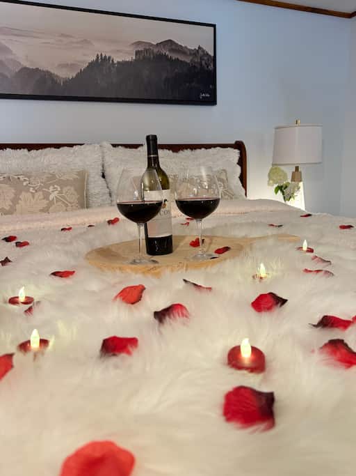 A wooden serving tray with a bottle of red wine and two glasses sitting on a bed covered in red rose petals for a romantic Vermont winter getaway
