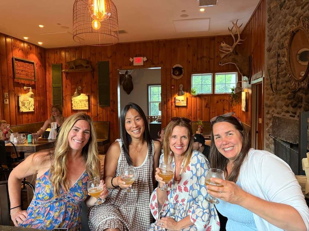 A group of women holding up their drinks at Mad River Barn in Waitsfield, Vermont during a girls' weekend getaway.