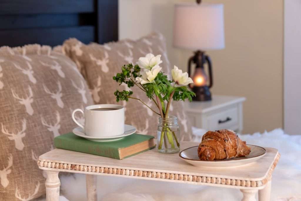 A tray with fresh coffee, a book, and a croissant on a bed at our Vermont lodging