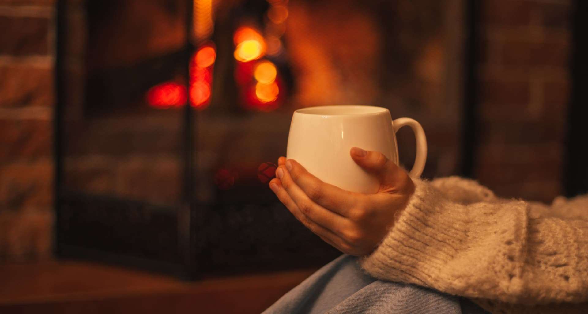 A woman holding a cup of coffee next to the cozy fireplace during a Vermont winter Hygge Lifestyle-inspired getaway